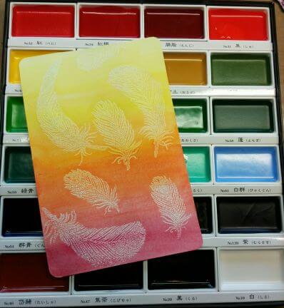 Gansai Tambi Sets featuring vibrant watercolor paints and a feather illustration on a gradient background.